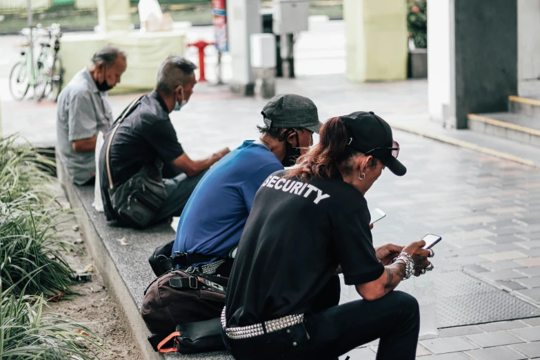 four men are sitting in line on the sidewalk