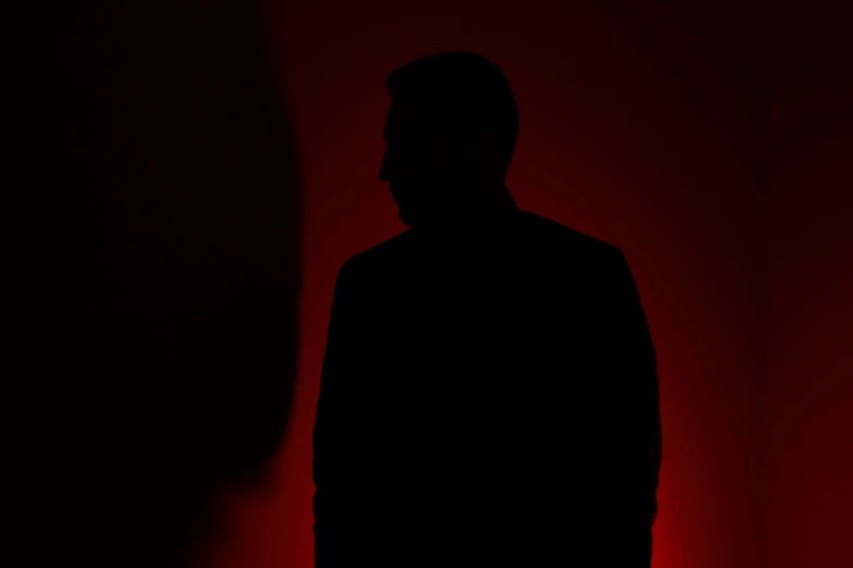 man standing in dark room with red light coming from behind