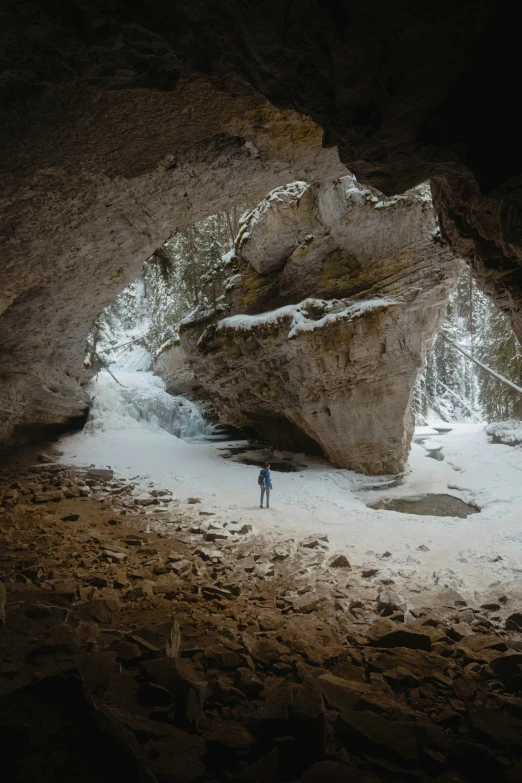 a lone person in a winter scene looking into a cave