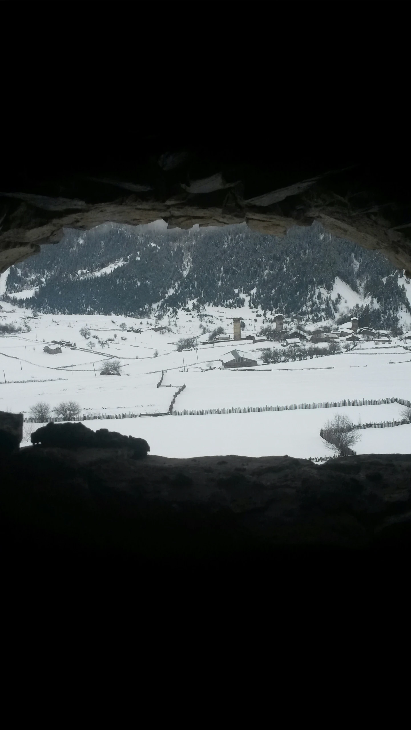 the view out of a cave into a snowy valley
