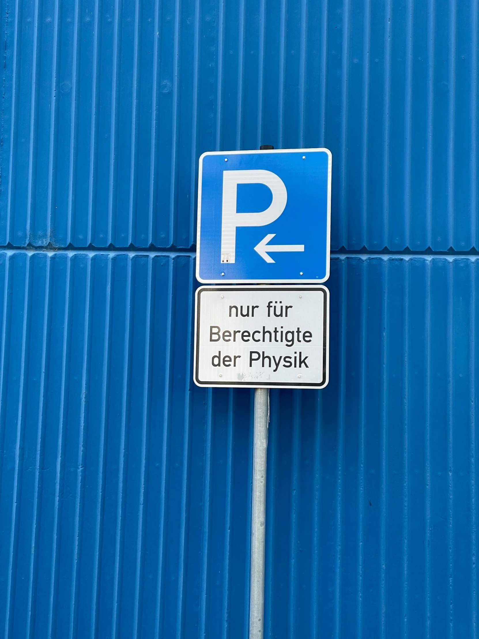 two different street signs on a pole against a blue wall