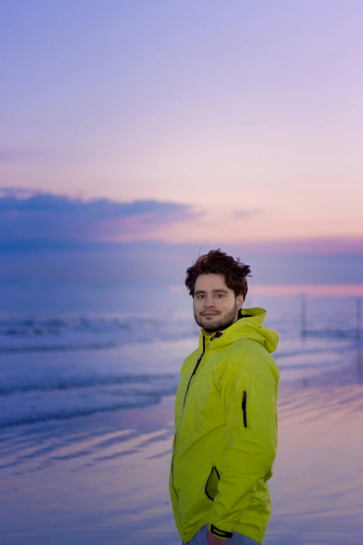 a man wearing a bright yellow jacket stands on a beach at sunset