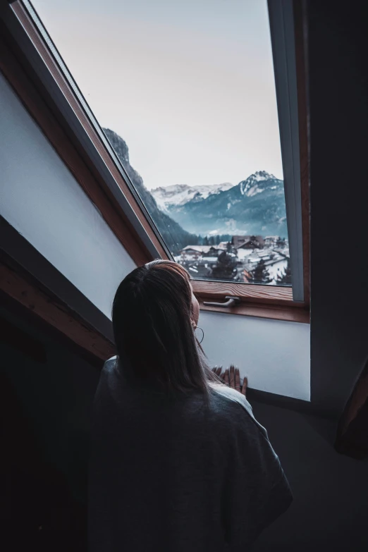 a woman standing in front of a window overlooking mountains