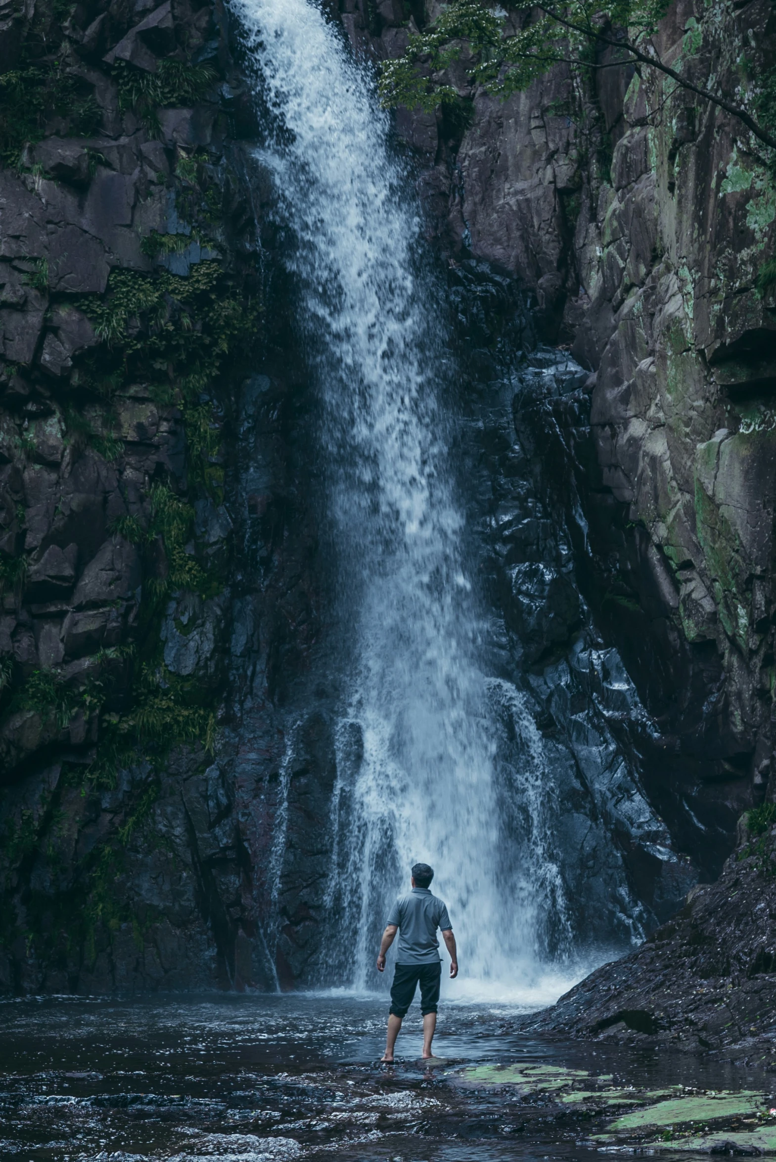 the man is standing in the water near the waterfall