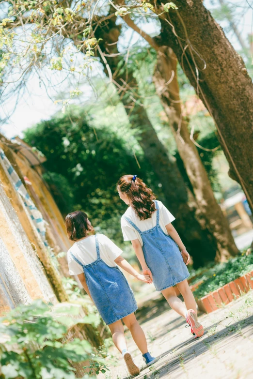 two girls walk past a bunch of trees in a park