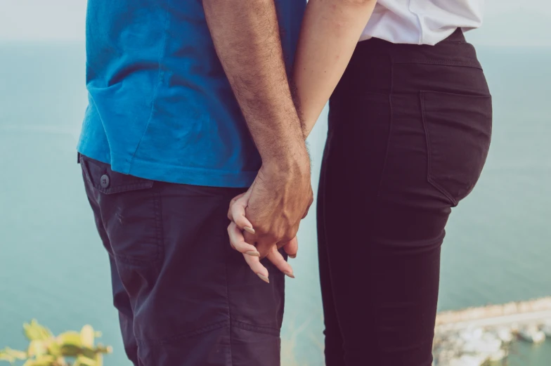 two people stand holding hands while facing away from the ocean