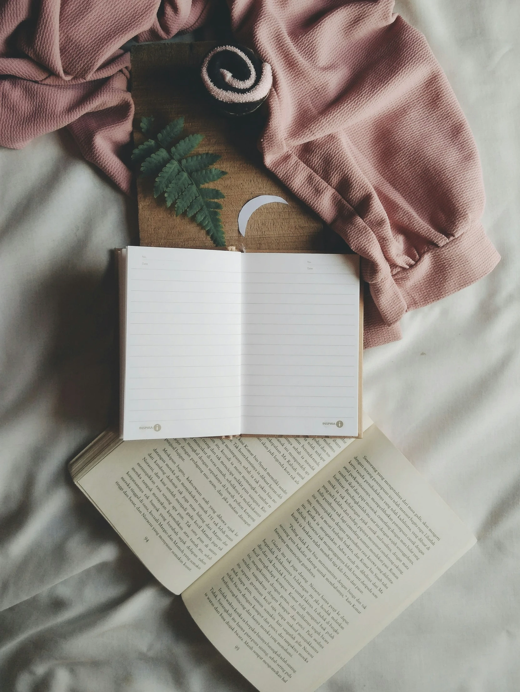 an open book, notepad and an alarm clock on a bed