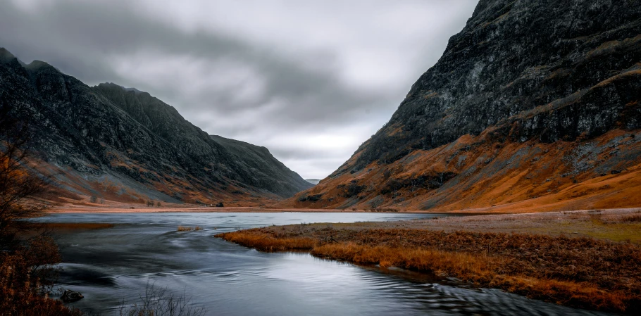 a lake surrounded by some mountains with water and grass