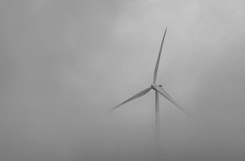 two windmills standing in the fog of a cloudy sky