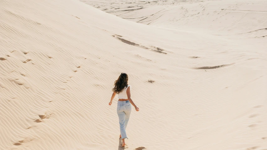 a woman is walking through sand with her long hair blowing in the wind