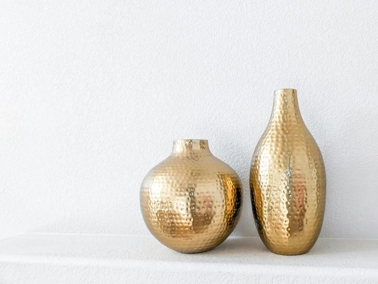 two golden vases on a white surface