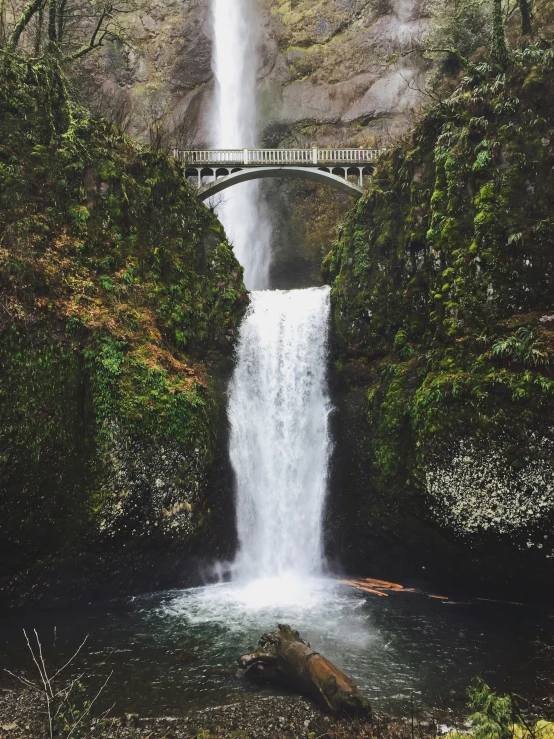 a large waterfall under a bridge in the forest