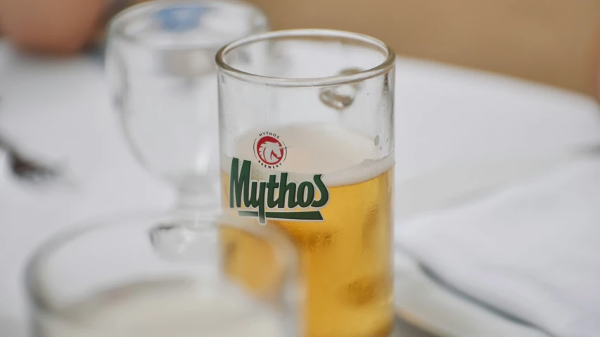 a glass full of beer next to a white plate and a silver utensil