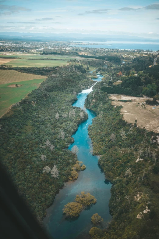 an aerial view of a river running between grassy land and forested area