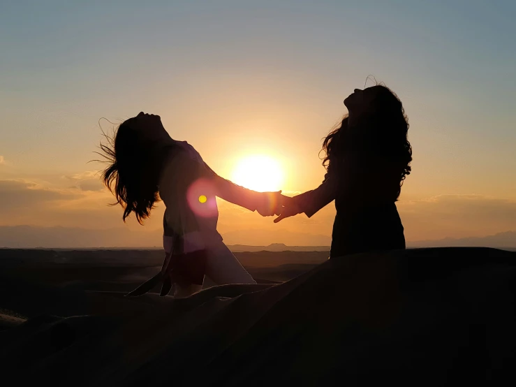 two girls holding hands with the sun setting behind them