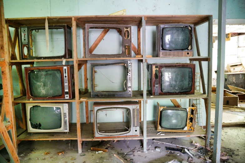 many old televisions in a messy room with wooden shelves