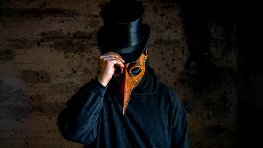 a man in a mask wearing a top hat holds up his sunglasses