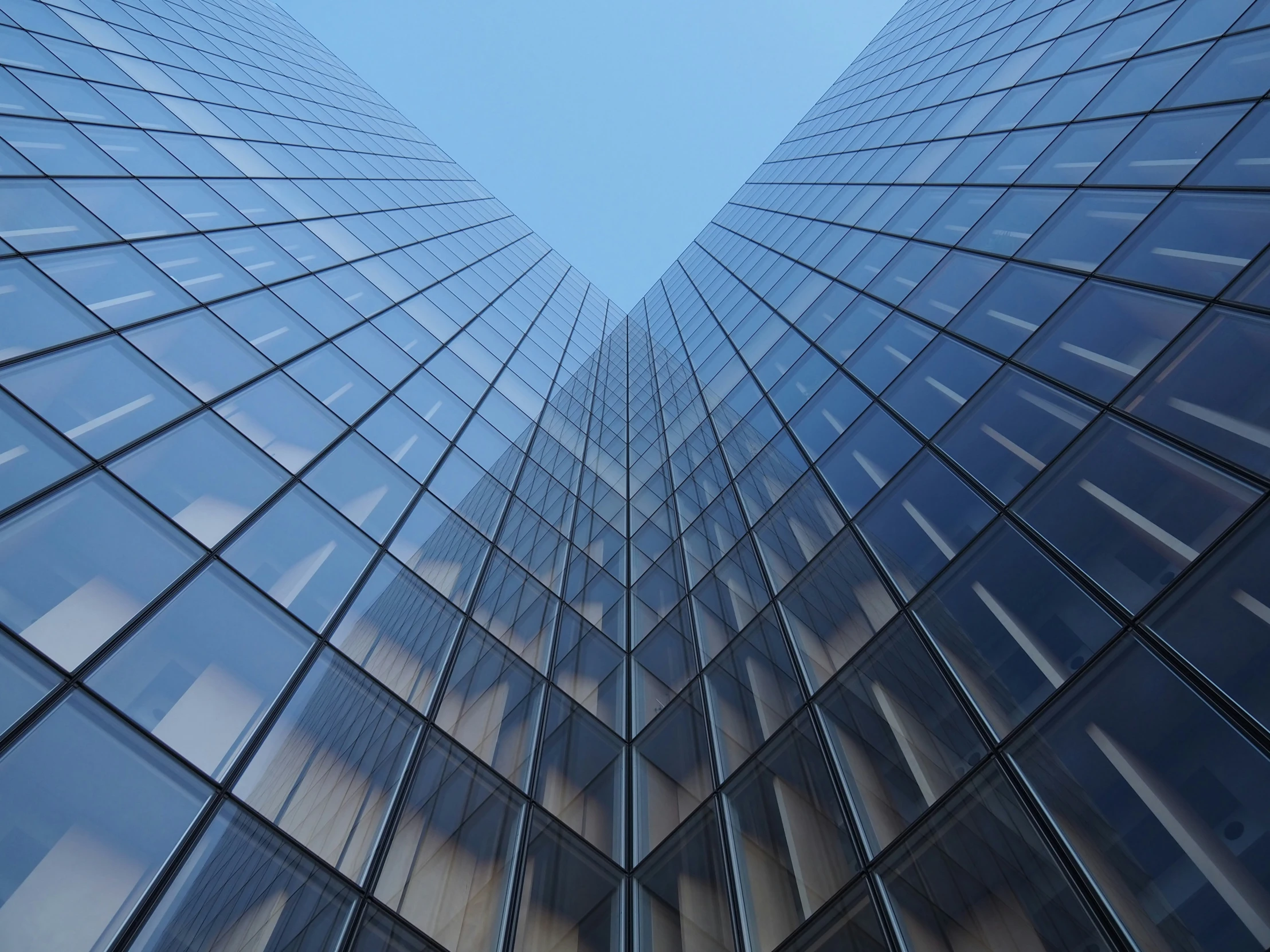 two tall skyscrs that have glass windows against a blue sky