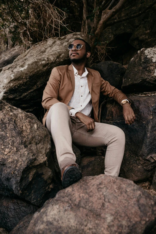 a man in sunglasses and tan jacket leaning on rocks