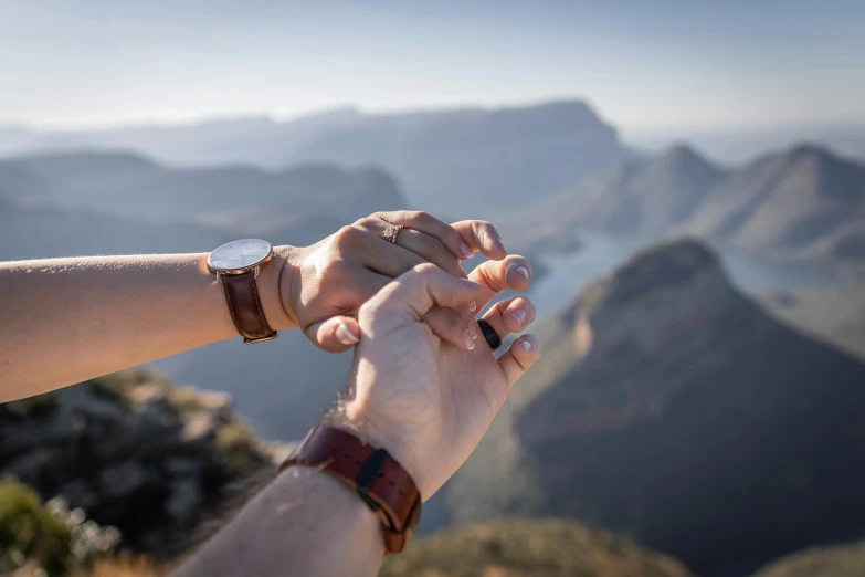 a man holding the hand of another person who is touching his hand on the top of a mountain