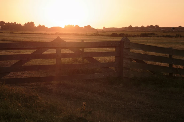a fence sits on the side of a field as the sun sets
