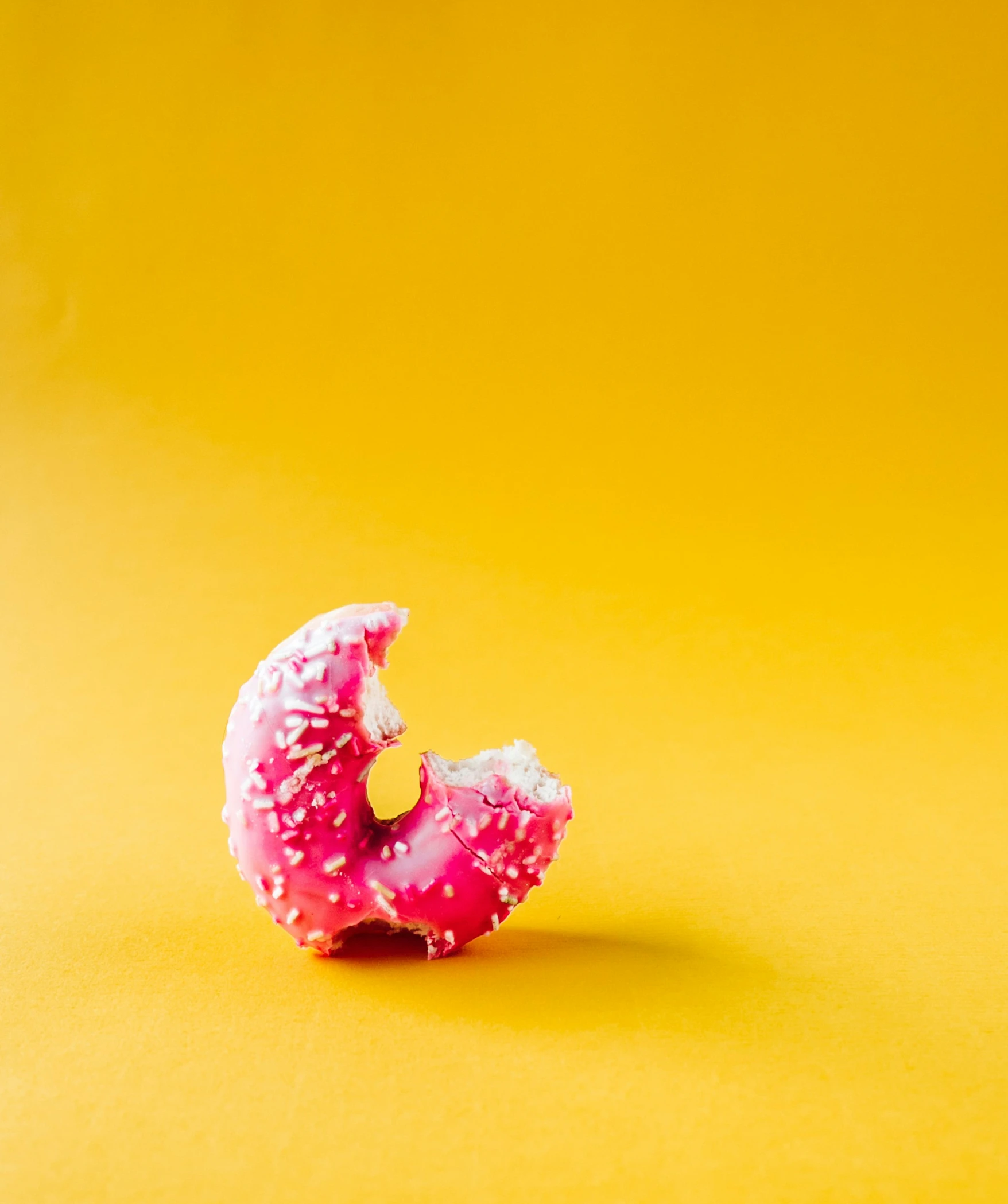 donut on yellow surface with pink frosting in middle