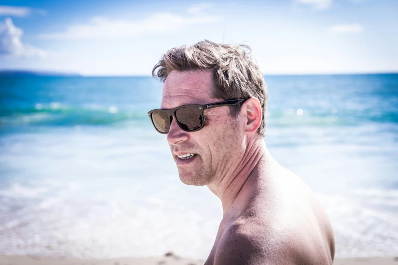 a man wearing sunglasses standing on top of a sandy beach