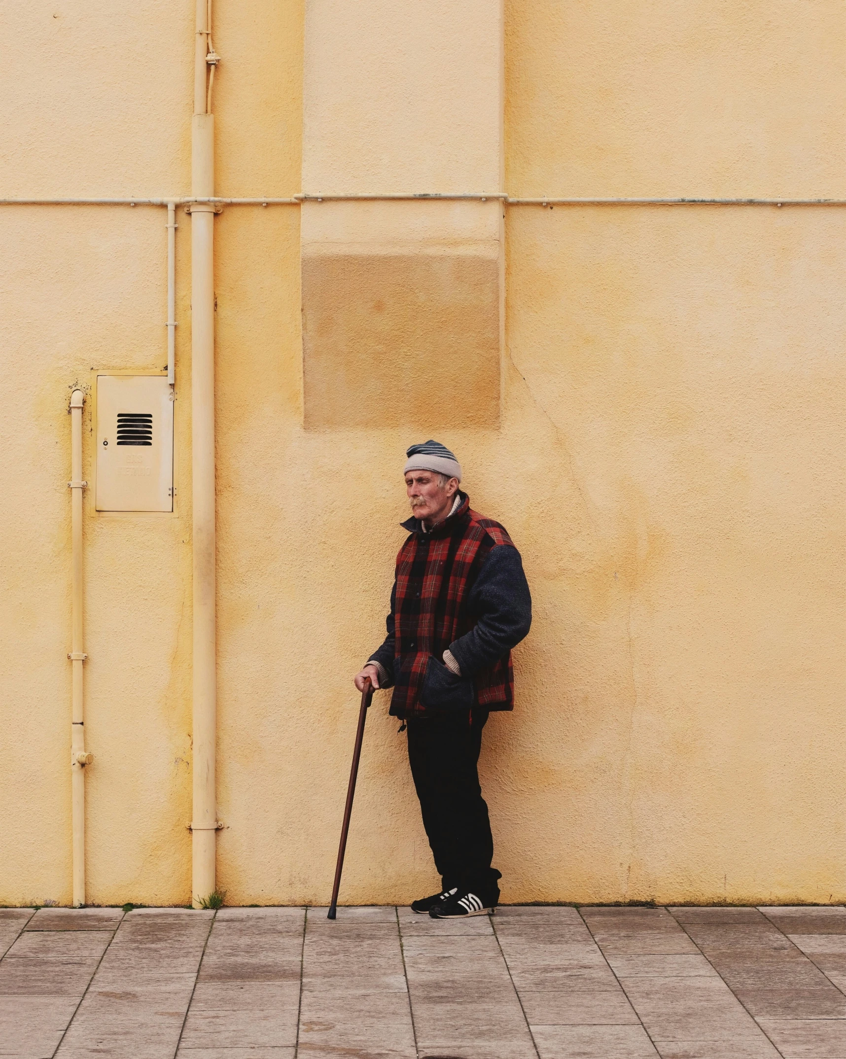 a man wearing black and red is leaning against a yellow wall