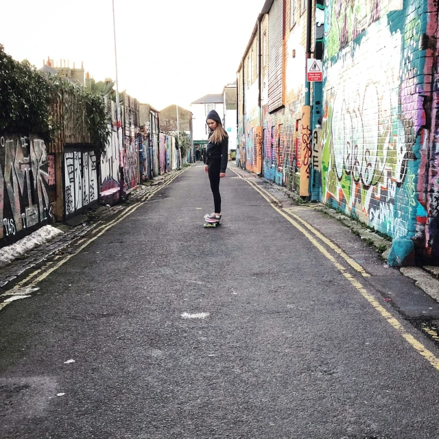 a woman skating down a street in a graffiti lined alley