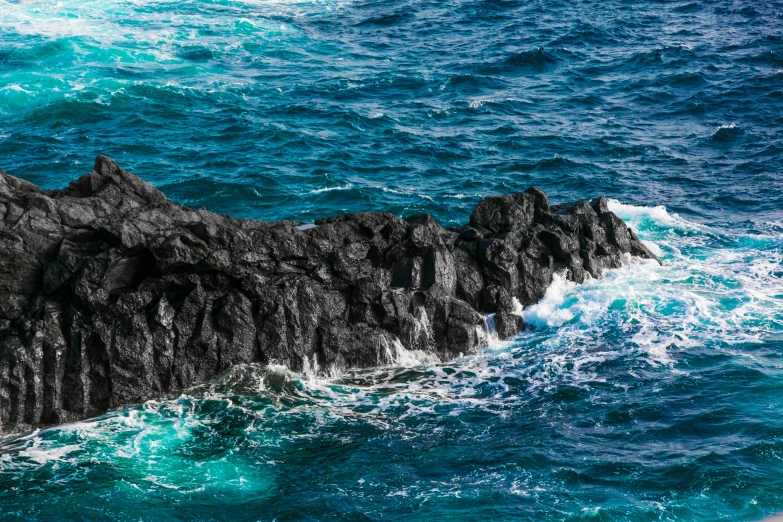 waves splash about black rocks on a blue ocean