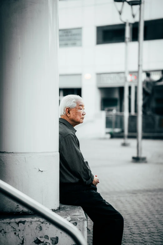 a man is leaning against a pole with a building in the background