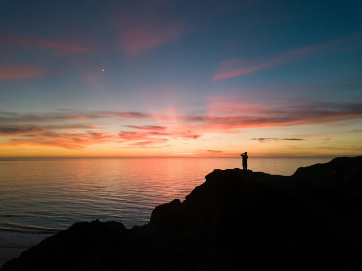 man standing on cliff near ocean watching beautiful sunset