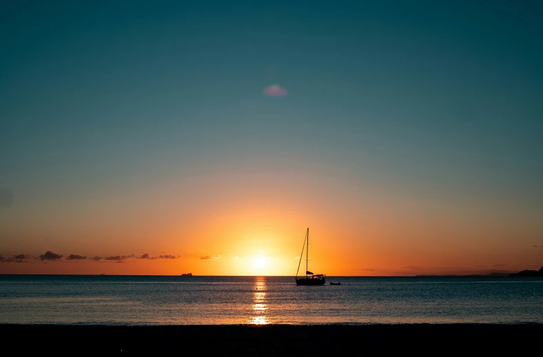 a sunset over the ocean with a sailboat in the water