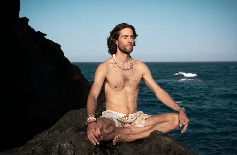 there is a man sitting on the rocks near the ocean