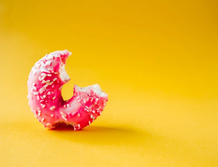 a pink glazed donut with sprinkles is on a yellow surface