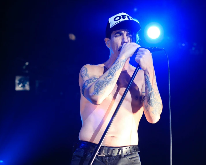 shirtless male in black pants singing into a microphone