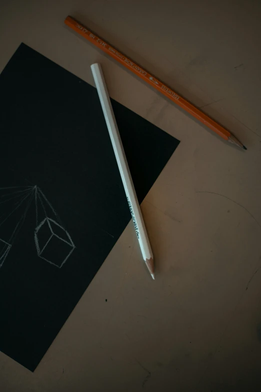 a pencil sits beside a black sheet with white shapes drawn on it