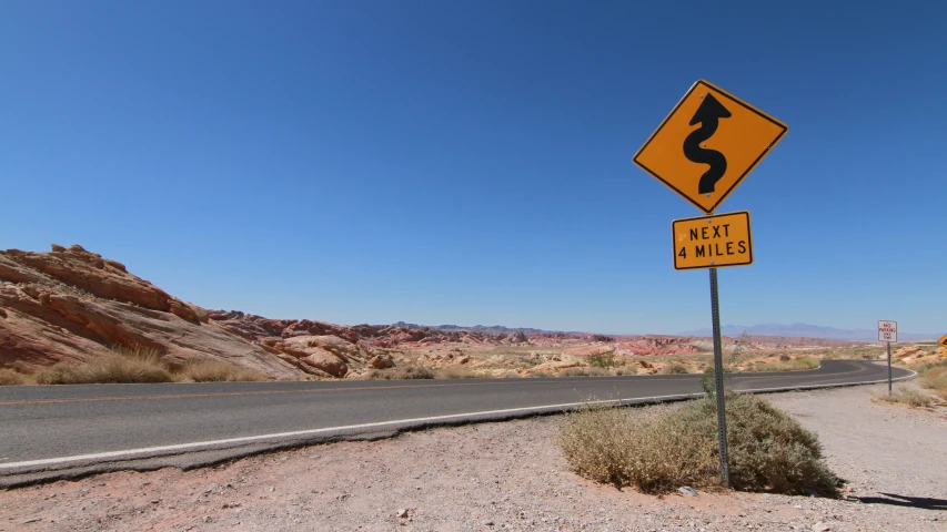 a road sign by a desert road with mountains in the distance