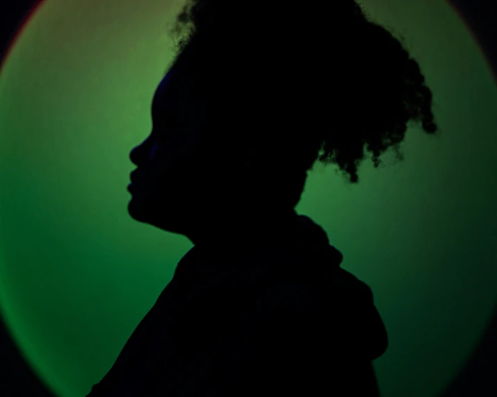 a profile view of a person with an afro hairdo and a green neon circle behind them