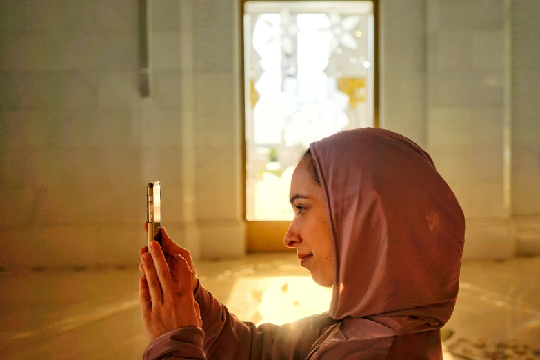 a woman in a muslim head covering looks at her cellphone