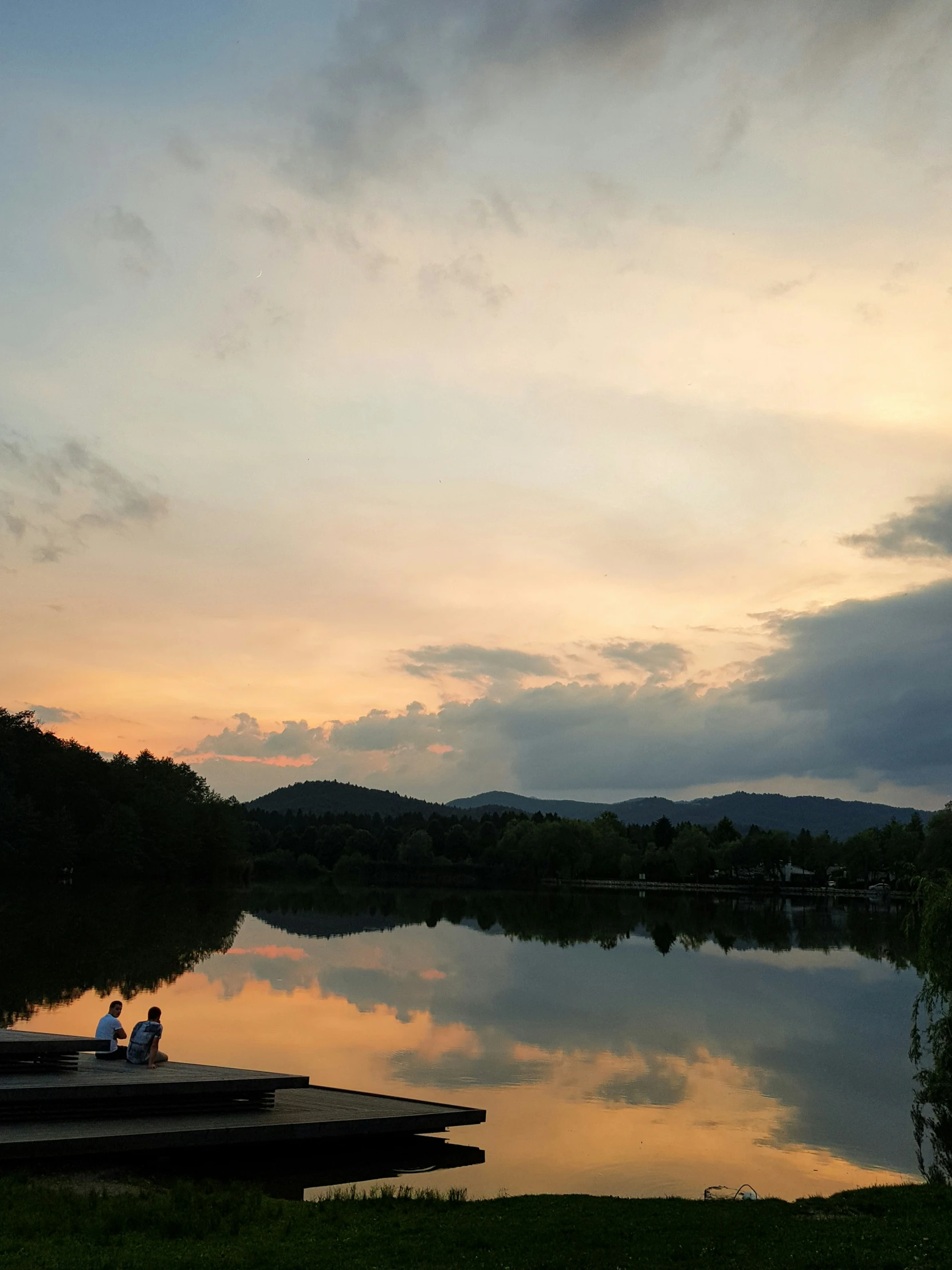 two people sitting at a dock overlooking a lake