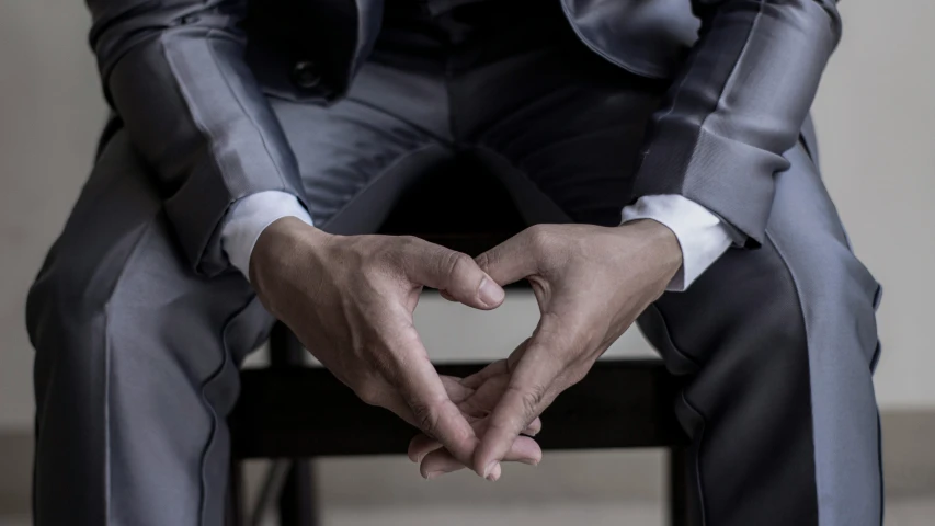 a man in a gray suit sitting down with his hands folded over his feet