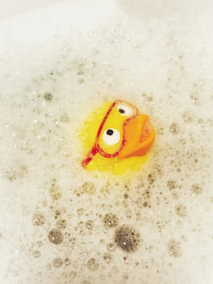 rubber duck sitting in bubble bath next to bubbles of water