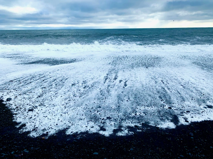 white snow covering a black beach under gray sky