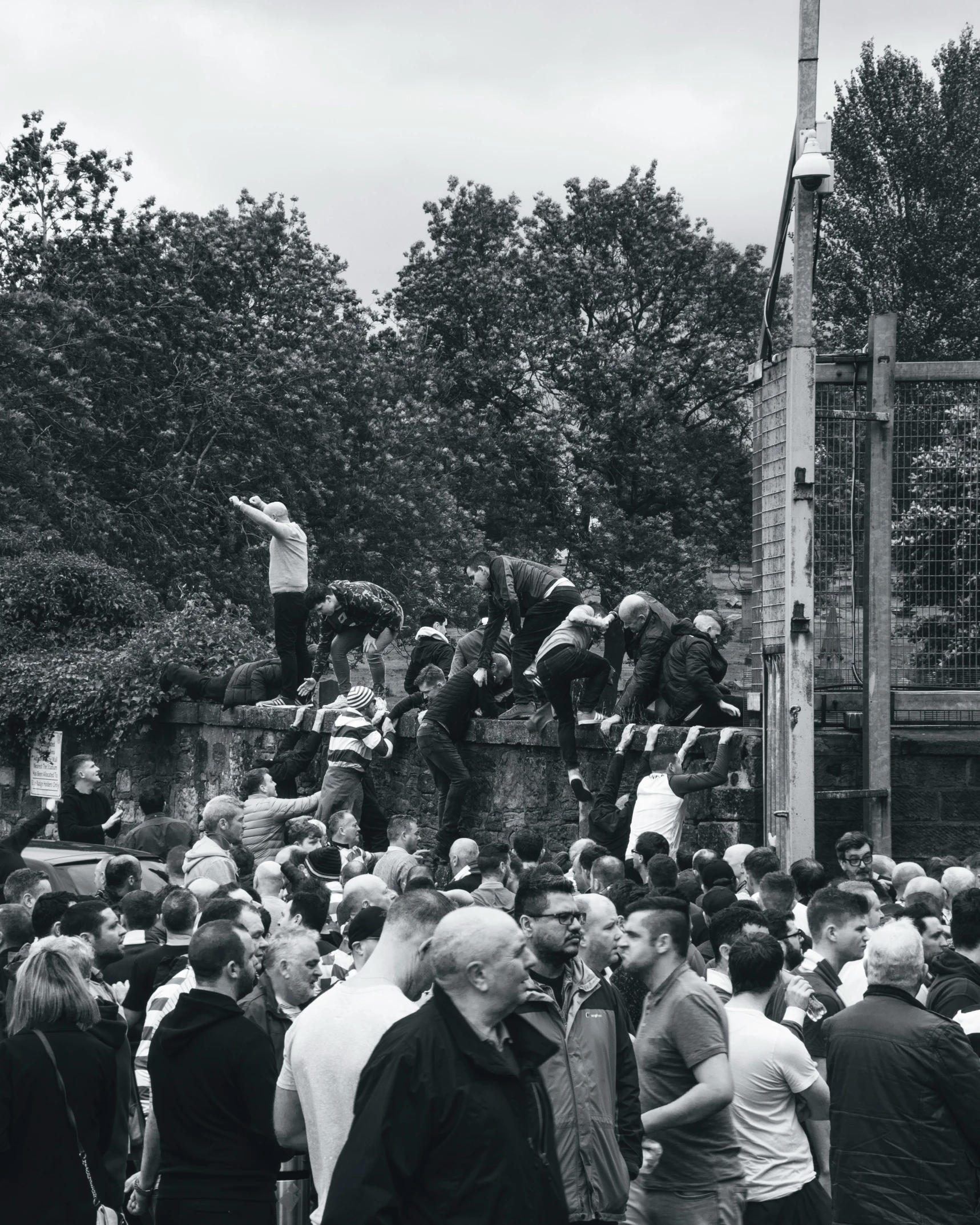 group of people standing near trees with man jumping over the fence