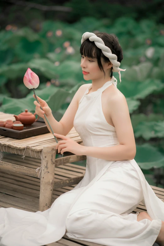 a woman in a white dress sitting on a bench with a rose