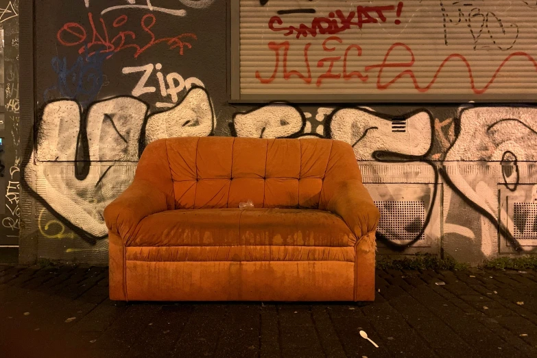 an orange chair sitting against a wall with graffiti