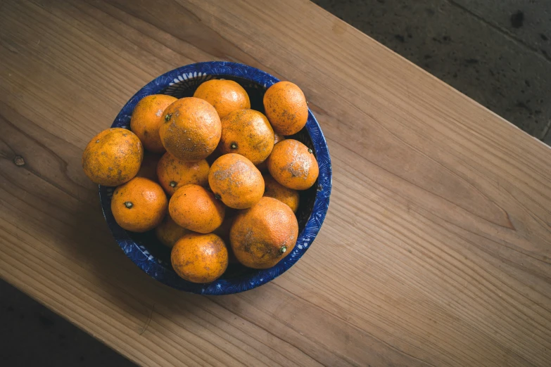 a blue bowl filled with oranges on top of a table