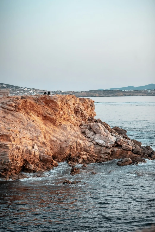 a beach next to the ocean with people sitting on rocks