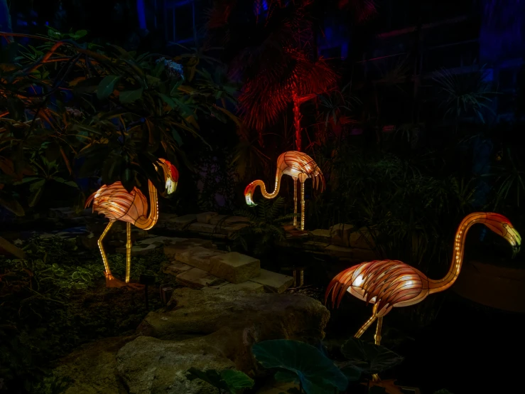 illuminated flamingo sculptures in a dark tropical garden